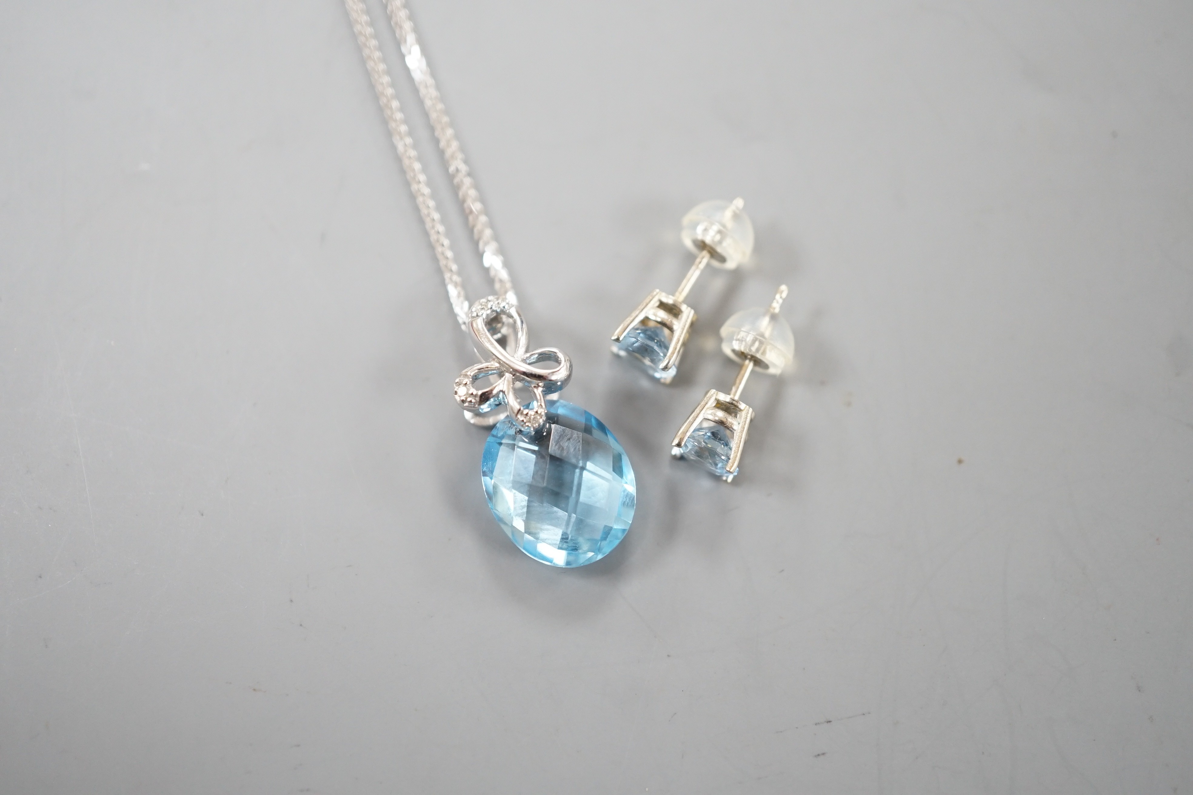 A modern 14k white metal, facetted pear cut blue topaz and diamond chip set pendant, 19mm, on a 750 white metal chain, 44cm and a pair 14k and blue topaz ear studs, gross weight 5.1 grams.
